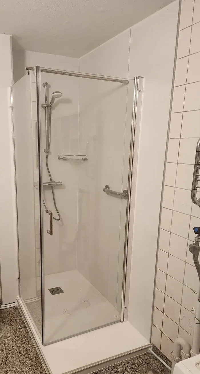 Dezelfde badkamer na verbouwing: ligbad vervangen door douchecabine met glazen deuren, steunbeugel en douchebak