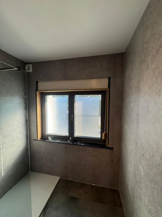 Badkamer rondom bekleed met grijze stenen-look wandpanelen, raam en inloopdouche met witte douchebak