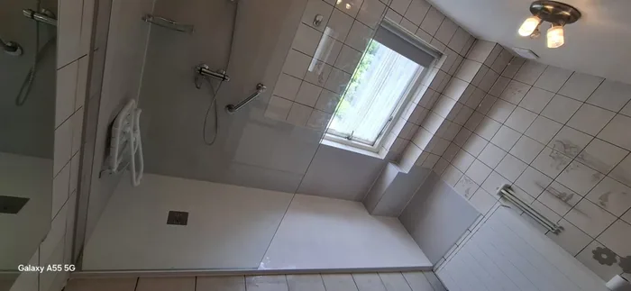 Brede inloopdouche bij het raam met douchezitje, steunbeugel en glazen wand