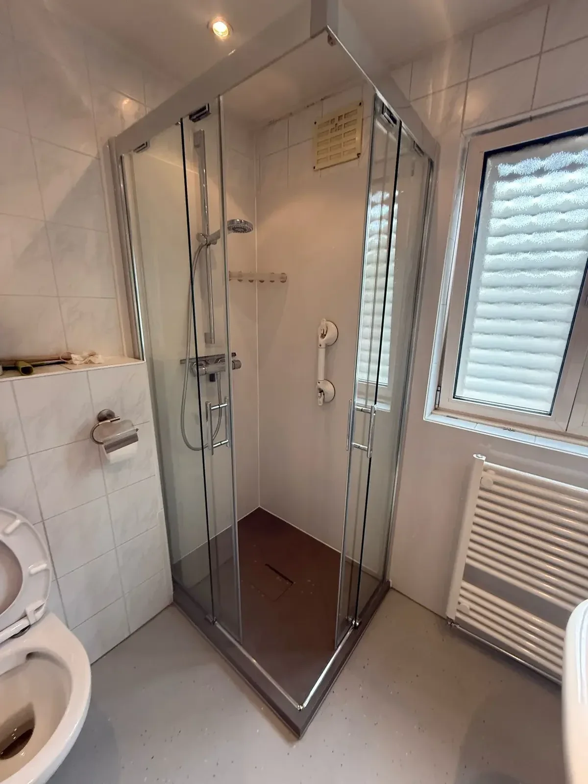Vierkante glazen douchecabine met steunbeugel, naast toilet en handdoekradiator