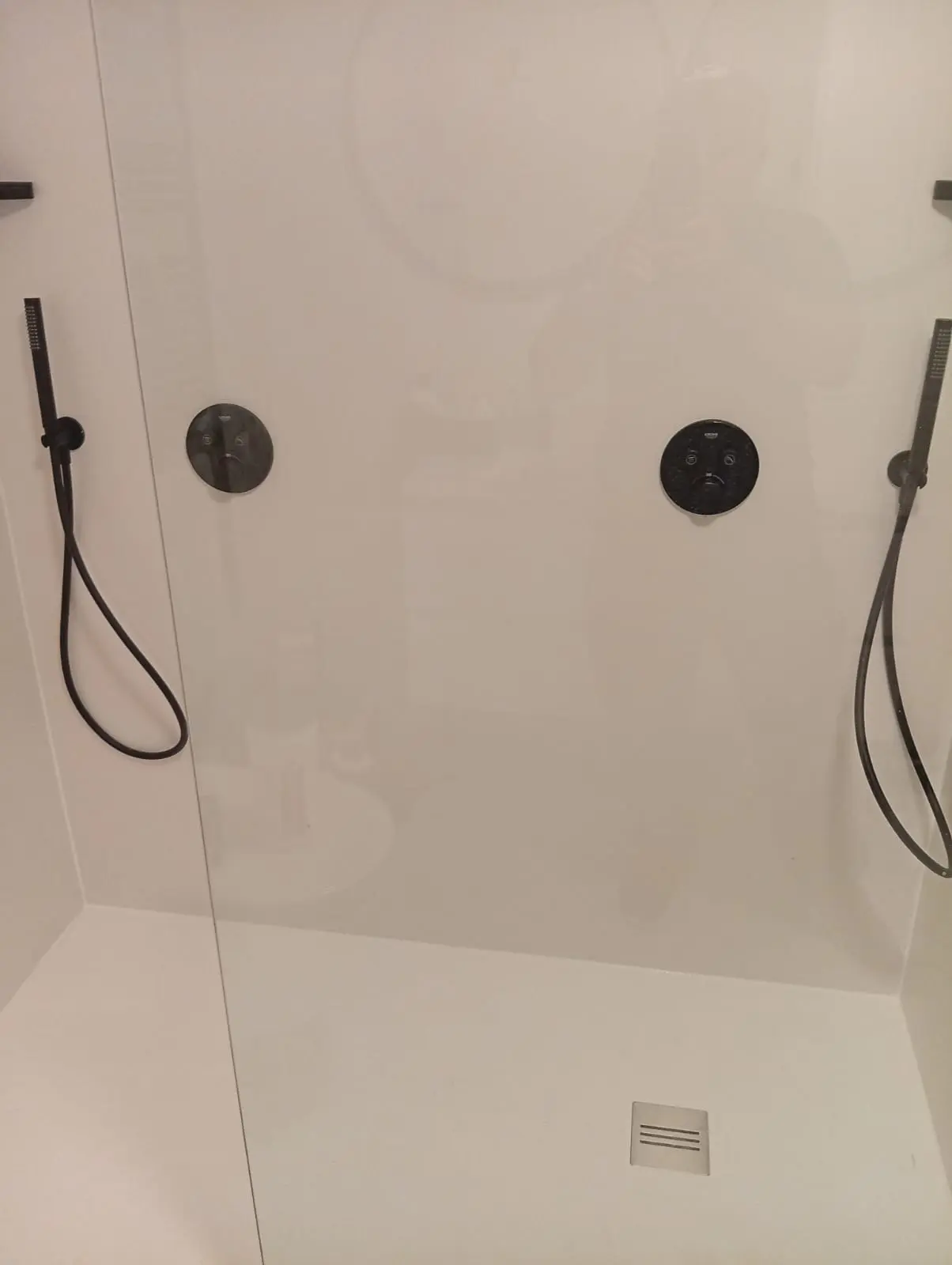 Strakke, drempelloze inloopdouche met witte wandpanelen en matzwarte Grohe kranen, ideaal voor senioren.